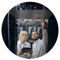 Two employees working in server room pointing to technology devices