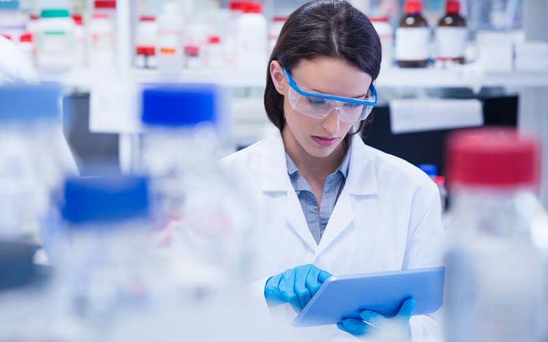 Female scientist works in lab surrounded by medication on tablet device