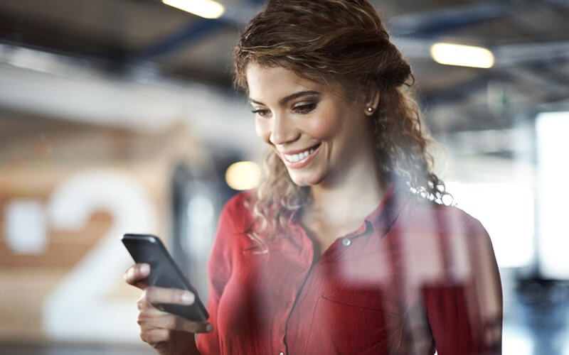 Smiling woman uses mobile phone in modern workplace