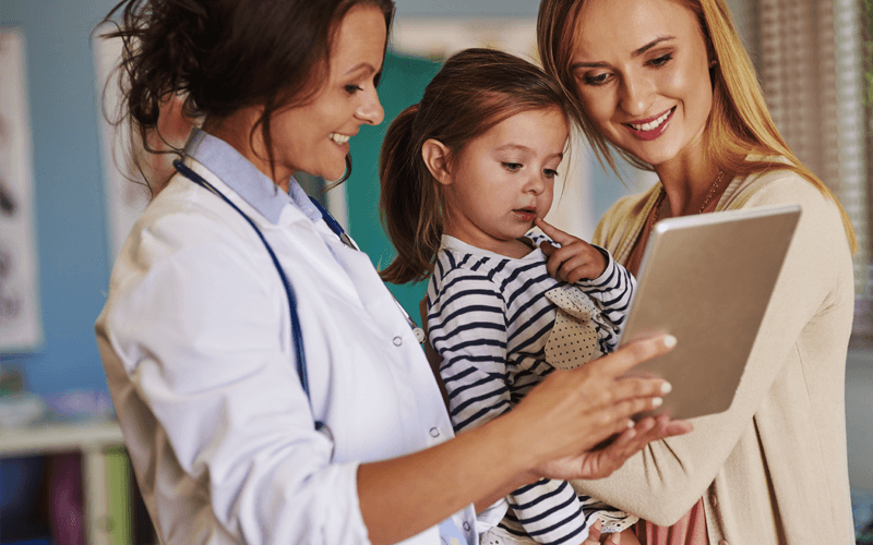 Doctor with child patient and mother showing tablet device