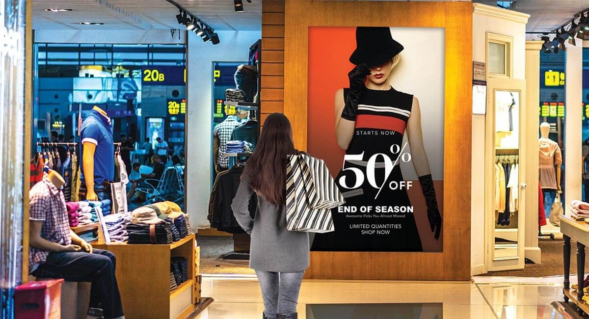 Woman holding shopping bags faces a promotional sale banner outside of a retail window