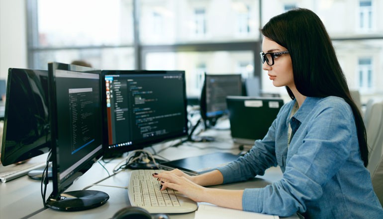 Female developer works at desk with multiple monitors 