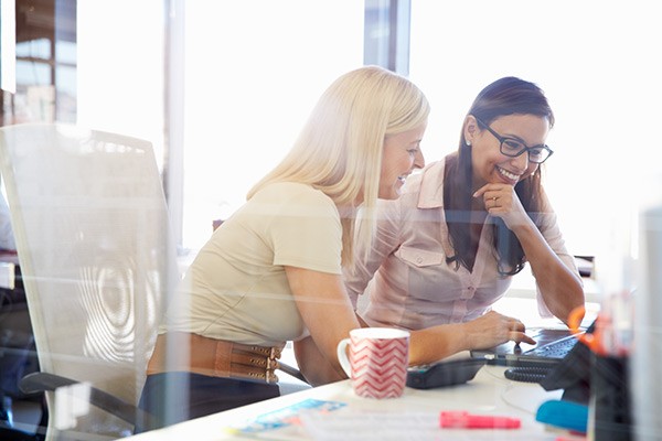 Global Knowledge Curriculum Women at a desk smile and discuss work