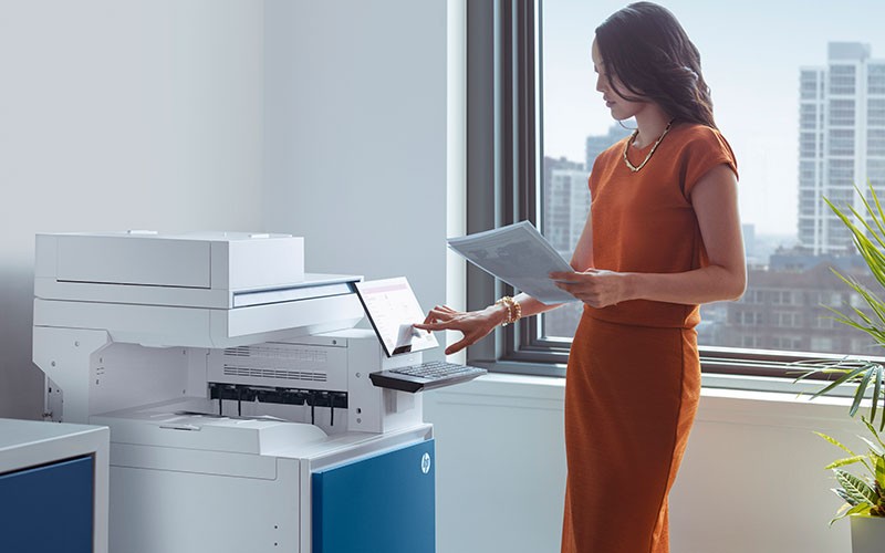 HP LaserJet Enterprise Flow MFP M527z at a print station in an office setting using an HP Pro Tablet 608 G1 to print color output
