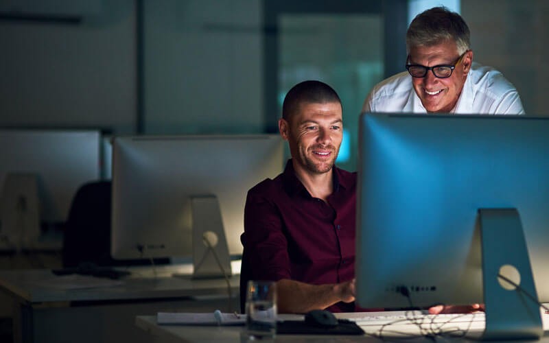 Two men smiling while working on monitor