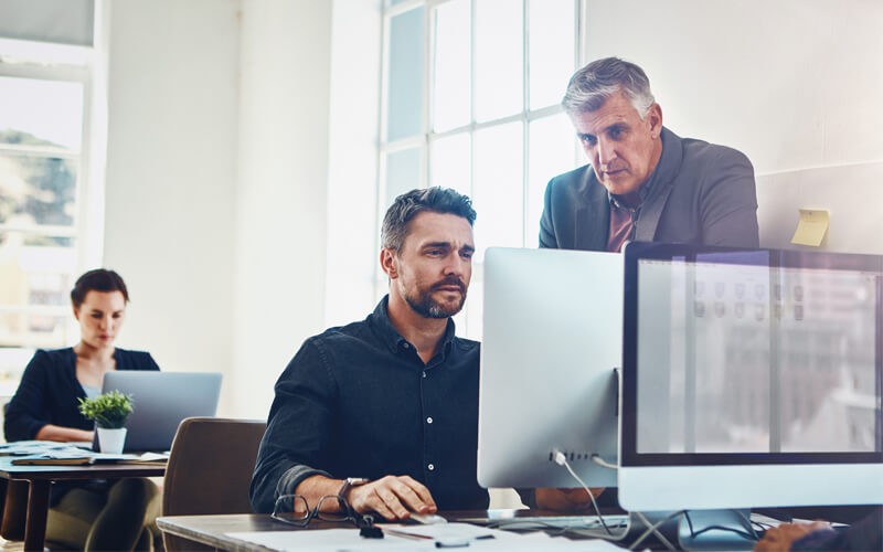 One Identity asset and identity management solutions Two men working at desktop monitor