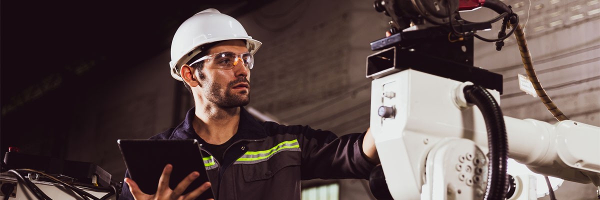 Man in hard hat works with manufacturing robotics technology with tablet device