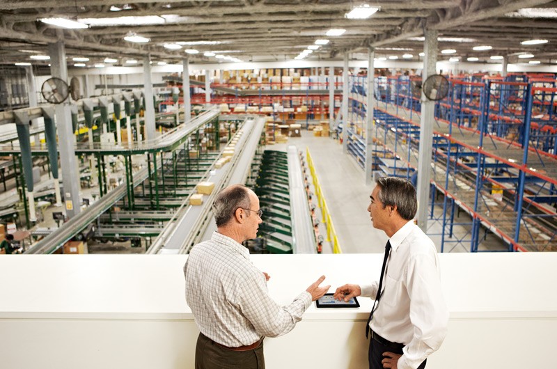 Two men in industrial warehouse talking.