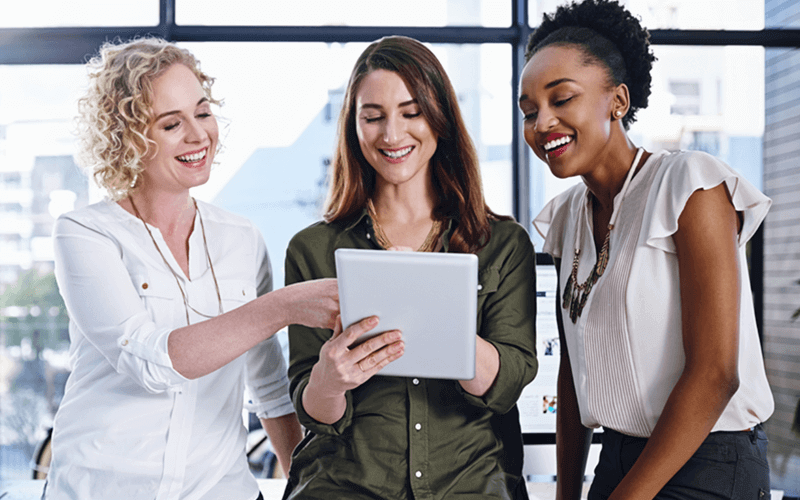 Three business women in front of open office window on tablet device