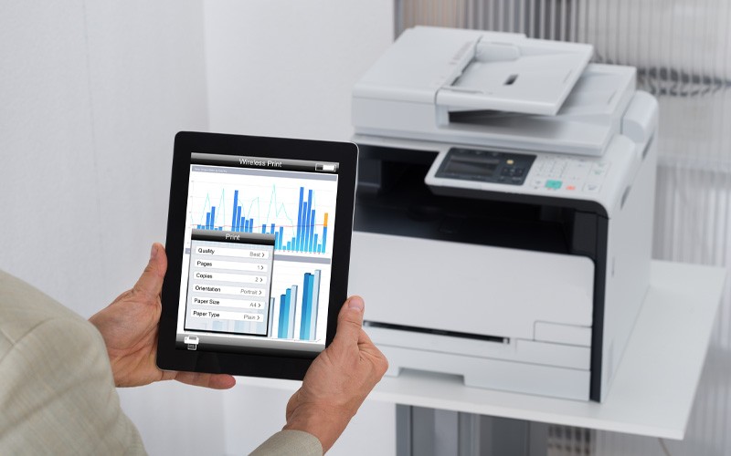 Woman holding tablet with data up in front of printer